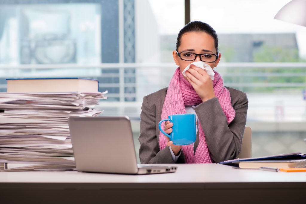 Sick woman at desk with mug and tissue on nose